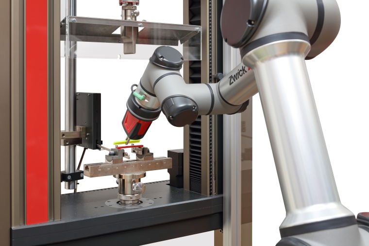 Der Roboterarm von RoboTest N beim Einlegen einer Kunststoffprobe für eine...